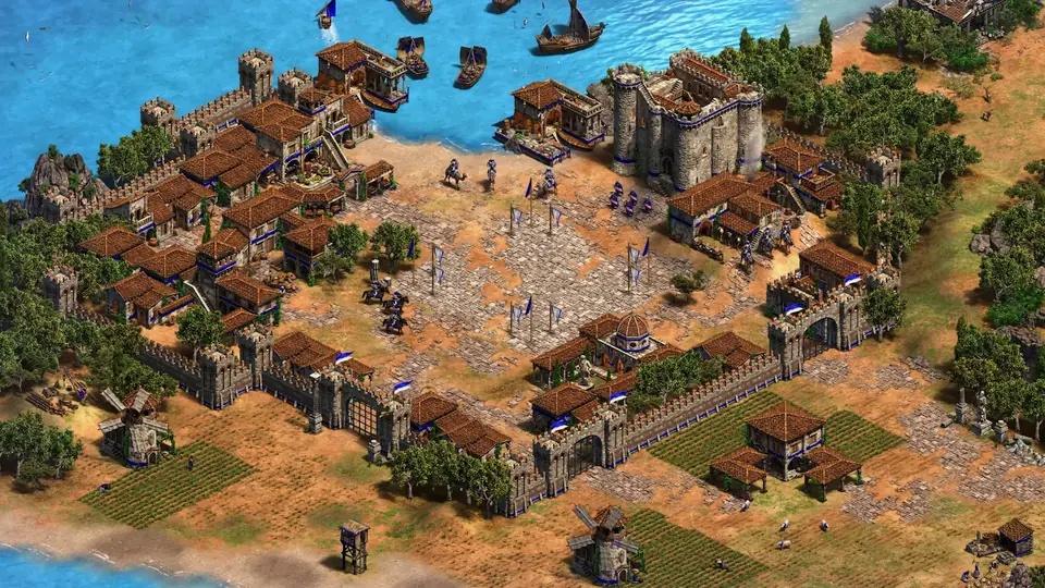 Age of Empires II: Definitive Edition: a walled medieval town with a castle, farms and windmills beside a bay with ships